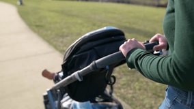 Mother pushing a stroller with a child, rear view with green sweater and jeans at the park