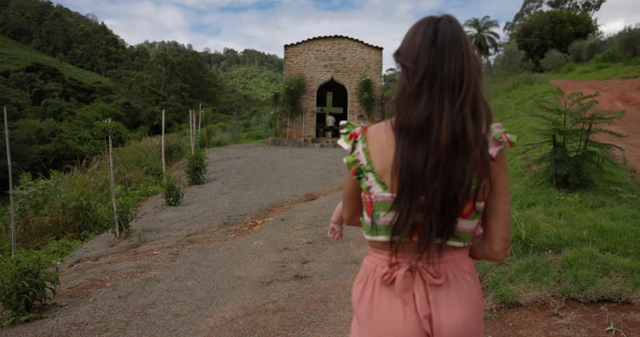 Young mother bringing her young daughter to small church on hill top in tropical location