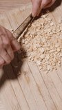 Vertical video. Ingredients for granola are spread on the table, and a woman is seen from a top-down view chopping peanuts.