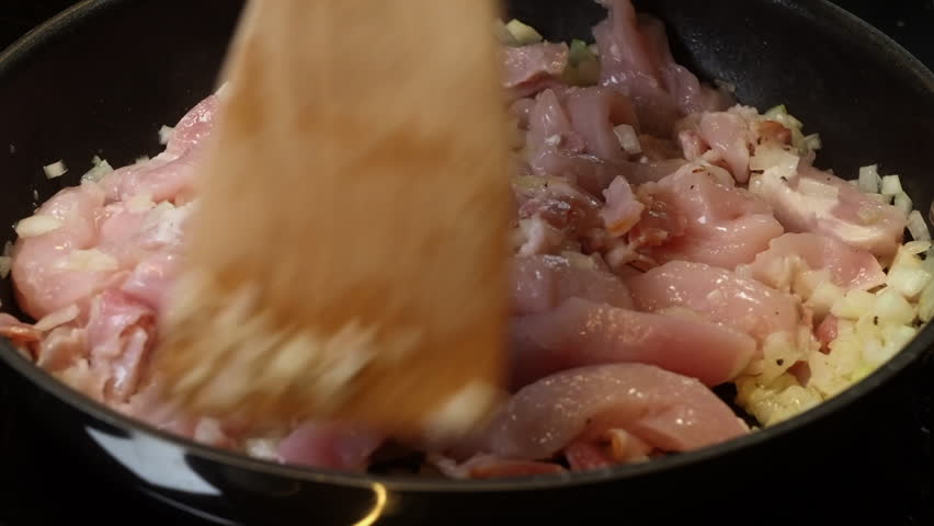Raw chicken breast added to frying onions in hot pan on stove, closeup