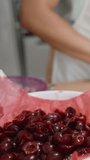 A plate with pitted cherries is in the foreground, which the woman takes and places the cherries onto the dough. Vertical video.