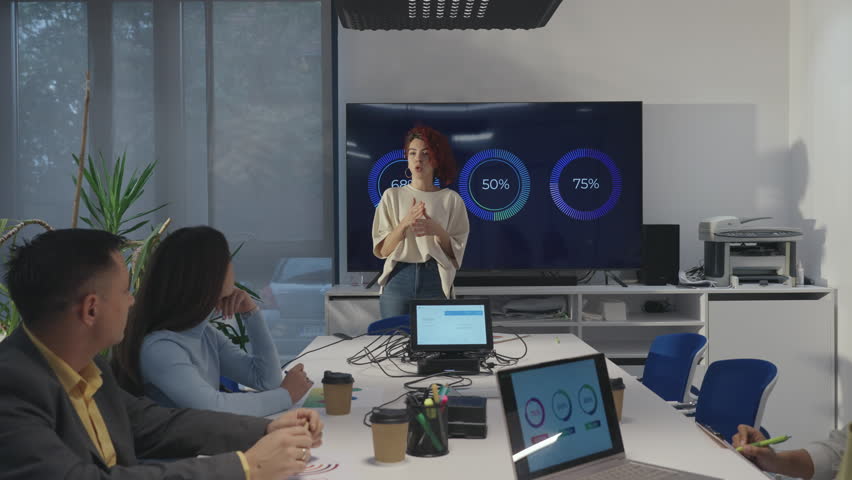 Portrait of a hispanic woman team leader presenting project in a boardroom during a meeting. Latino business woman standing in front of a big screen in an office and talking about sales numbers.