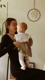 a mother throws a baby girl into the air. a girl in a dress in her mother's arms. the family is playing at home. vertical video