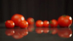 One by one, large tomatoes fall onto the wet surface, forming splashes. Tomatoes of different sizes are beautifully laid out on a dark table. High quality FullHD footage