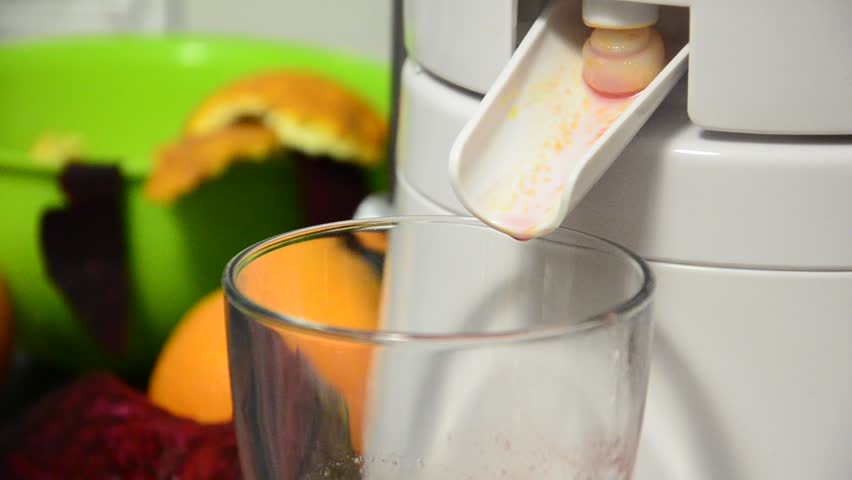juicer fillS up the glass with fresh healthy orange and beetroot juice