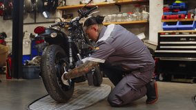 Side view of multicultural mechanic in gray uniform checking tires of motorcycle with wrench while working in repair shop - Powered by Shutterstock - Get 15% off with code: PIKWIZARD15