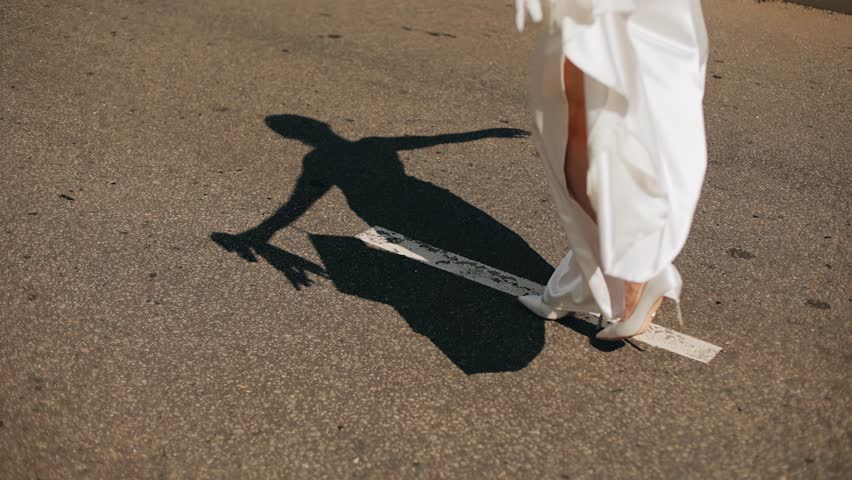 A girl walks in a dress in the center of the road with her arms spread. Her shadow falls beautifully on the asphalt Royalty-Free Stock Footage #3473252025
