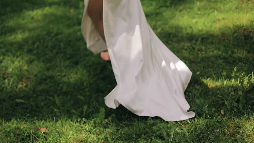 A girl in a long white dress runs through the grass. Shooting her legs in slow motion Royalty-Free Stock Footage #3473252091