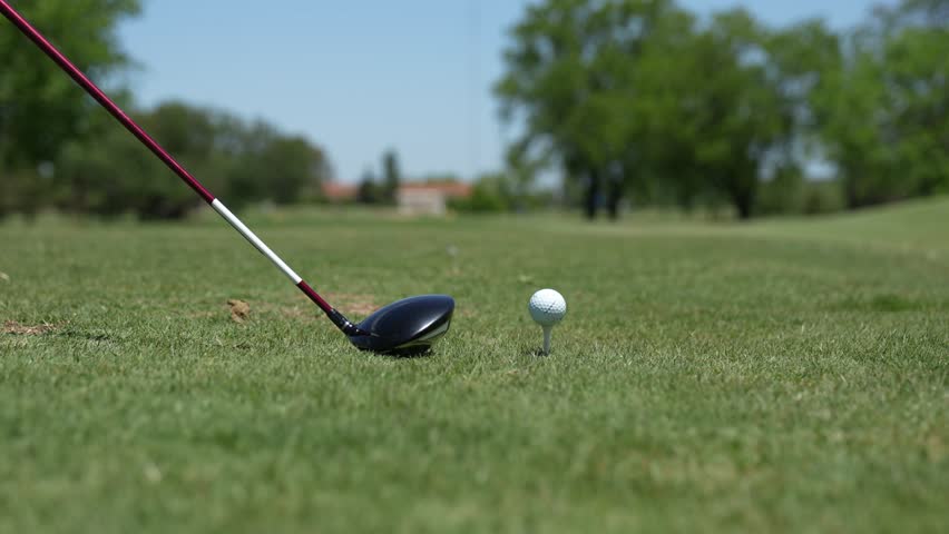 A close-up of a golf club and ball placed on a tee, with a lush golf course as a backdrop. ready to take a swing.