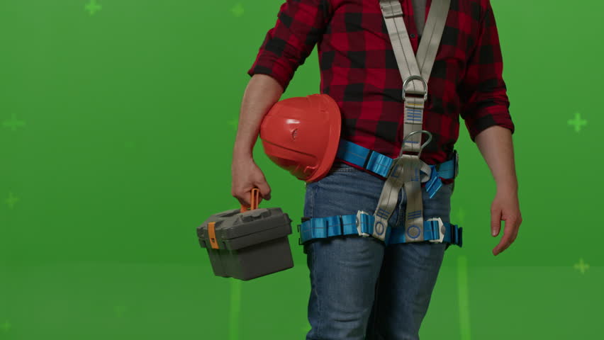 Close-up of side view of male builder with professional ammunition walking on a green background