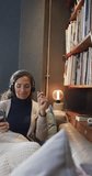 Vertical video of biracial woman listening music using smartphone in living room, slow motion. Lifestyle, free time, relaxation, communication and domestic lifestyle, unaltered.
