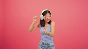 Young asian woman dancing music using a wireless headphone and a streaming cellphone app at red backdrop. Joyful chinese teenage female listening a song with earphones at pink color background wall - Powered by Shutterstock - Get 15% off with code: PIKWIZARD15