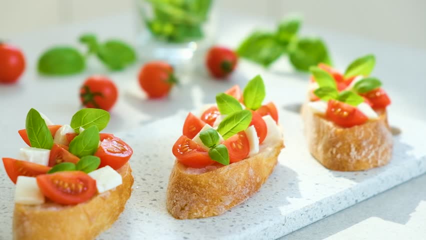 Bruschetta with cherry tomatoes, mozzarella cheese and basil in sun rays on marble board. Traditional Italian appetizer, snack or antipasto. Vegetarian food. Healthy eating. Mediterranean food.