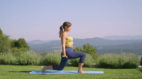 Woman in yellow top is practicing yoga pose in the garden when she loses her balance and falls just as her cute dog walks by. Young lady is focused on her perfect yoga posture to regain core strength. Stock video