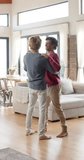 Vertical video of happy diverse gay male couple dancing in living room at home, slow motion. Lifestyle, togetherness and dometic life, unaltered.