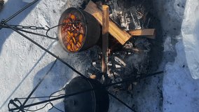 vertical video. cooking outdoors in winter. They cook soup in a pot over a campfire