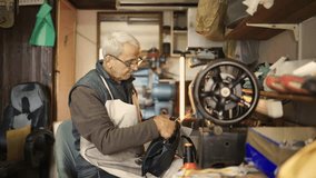 Side view of a senior shoemaker sitting at cobbler's workshop and sewing a leather purse. An old artisan is sitting at sewing machine and using it for repairing a purse. Senior craftsman at his shop.
 - Powered by Shutterstock - Get 15% off with code: PIKWIZARD15