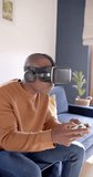 Vertical video of african american man using vr headset and playing video games at home, slow motion. Lifestyle, technology and domestic life, unaltered.
