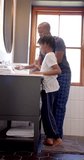 Vertical video of african american father and son brushing teeth in bathroom at home, slow motion. Fatherhood, childhood, togetherness, self care, hygiene and domestic life, unaltered.