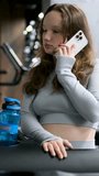 young girl in a gray tracksuit gymsuit In a dark gym, dissolve hair, headphones, exercise, take care of figure, of your health, drink water, set video set of video. Slim body. Happy workout. Cardio
