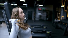young girl in a gray tracksuit gymsuit In a dark gym, dissolve hair, headphones, exercise, take care of figure, of your health, drink water, set video set of video. Slim body. Happy workout. Cardio