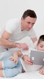 family in white bed with tablet examining game father showing how to press buttons correctly mother and son smiling laughing rejoicing child learning new game developing lessons cheerful family love