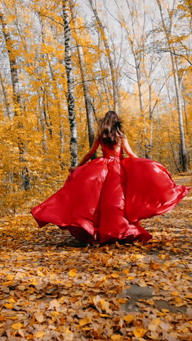 Girl in a red dress in the runs with the picturesque autumn landscape. Golden leaves, autumn forest.