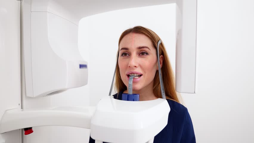 Female patient at panoramic x-ray shot of jaw holding face at x-ray machine. Woman standing in dental x-ray unit laser precise projection for dental radiography. Examining teeth in the modern clinic.