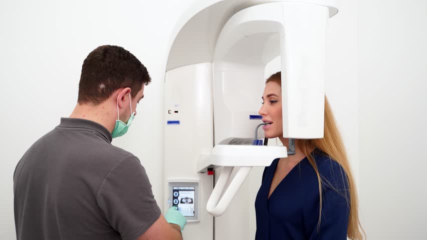Male radiologist taking teeth x-ray of female patient using dental x-ray machine. Dentist adjusts scan projection by laser guide. Doctor doing digital x-ray tooth scan for woman in the dental clinic.
