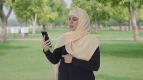 Muslim woman talking on video call in park