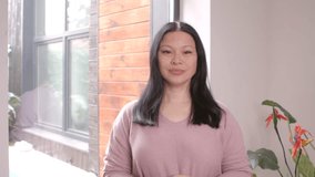 Confident beautiful middle aged Asian woman recording video content , communicating and sharing with online audience professional opinion and advice while standing in domestic room,