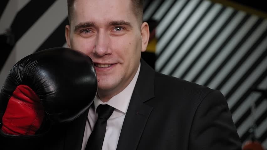 Close-up of a successful happy businessman in boxing gloves, boxing in the ring after a long working day in front of the camera.