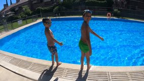 Slow motion video of happy boy of 7 years old and his brother of 9, jumping, diving and playing in the water of a swimming pool in the summer, blue water, smiling, and funny way.