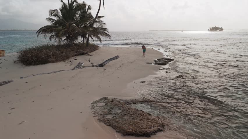 Dron close shot from a young man walking along a beach of a remote island in San Blas Archipelago, Panama.