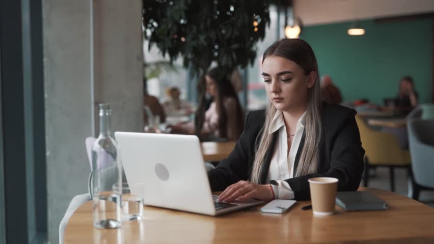 beautiful, sad young woman sits in a cafe in business attire, angrily closes her laptop, tapping on the table with her hand Royalty-Free Stock Footage #3473826575