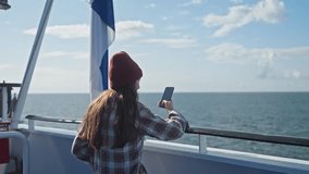 Woman sailing on cruise trip liner, girl standing on ship, taking pictures for social media, traveling on ferry, brunette in shirt and hat admiring ocean. Enjoying traveling and adventure. Finland - Powered by Shutterstock - Get 15% off with code: PIKWIZARD15