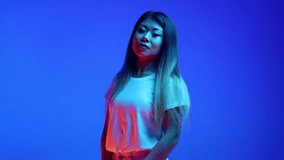 Confident, beautiful Asian woman, business lady posing looking at camera against blue gradient background in neon light. Concept of business, entrepreneurship, human emotions, self-expression.