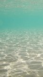 Vertical video, Sandy shallow water in sunburst and glare on sandy seabed, Slow motion. Sunlight passes through surface of turquoise water and glares on sand bottom in shallow water in sunbeams