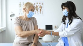 4K video footage of a doctor wearing medical face mask consulting mature woman patient at appointment in office, physician explaining treatment, giving recommendations, elderly generation healthcare