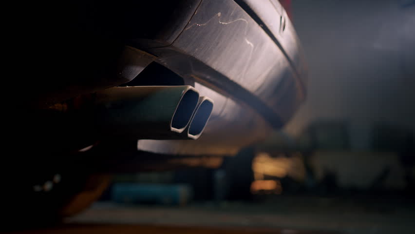 Close view of a car exhaust pipe, smoke comes out of the exhaust system of the car and pollutes the atmosphere. Environmental disaster of gasoline engines. Pros for protecting electric vehicles.