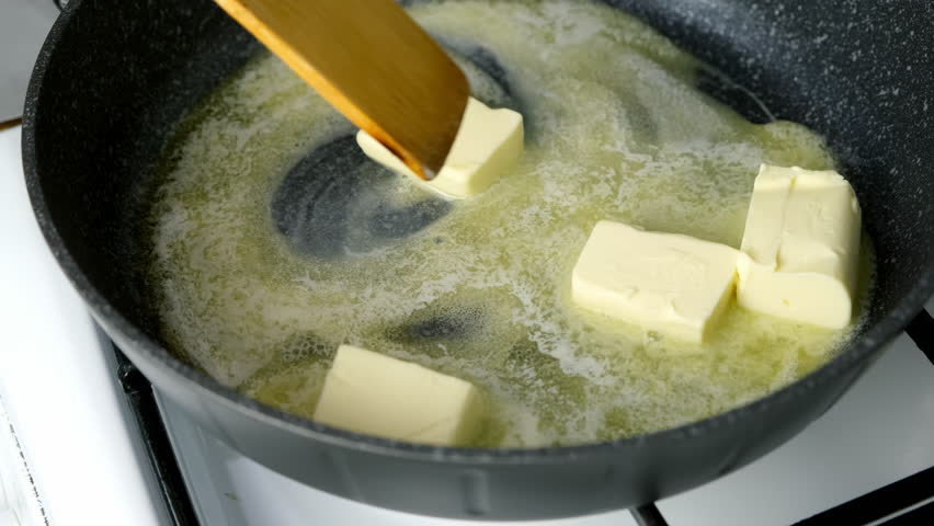 Woman cooking melting butter cubes on frying pan mixing with wooden spatula. Heating butter preparing dish. Cuisine culinary prepare cook dish domestic food recipe ingredients. Healthy nutrition.