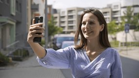 A beautiful young Caucasian woman shoots a vlog with her smartphone in a street in an urban area