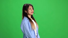 Surprised young Asian woman with open mouth looking at camera and holds hands raised against vibrant green studio background. Concept of human emotions, self-expression, fashion, style.