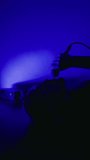 Studio recording: Rapper or singer male reclines, capturing vocals under electric blue light during music recording session
