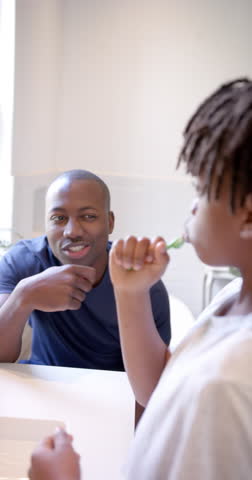 Vertical video of african american father and son brushing teeth in bathroom at home, slow motion. Fatherhood, childhood, togetherness, self care, hygiene and domestic life, unaltered.