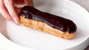 Eclair. Hand putting an eclair on white plate. Close up of woman's hand with chocolate eclair. Woman's hand putting eclair with chocolate icing on white plate, glazed dessert close-up - Powered by Shutterstock - Get 15% off with code: PIKWIZARD15