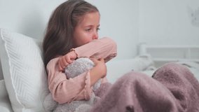 Upset sick girl coughing while sitting with soft toy on bed at home. Sad girl child suffering from cold and flu and using digital tablet in apartment. - Powered by Shutterstock - Get 15% off with code: PIKWIZARD15