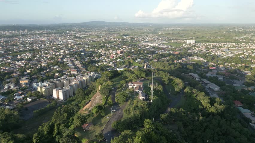 San Fernando Hill, Trinidad and Tobago. Aerial drone push-in shot over building facing Northern range on horizon. Soft evening light. Long shadows