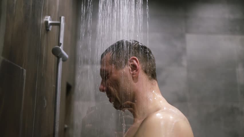 guy washes in the shower room after a soccer match after a workout, after training water runs down his face splashing water.