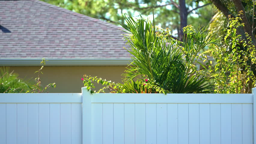White vinyl picket fence on green lawn surrounding property grounds for backyard protection and privacy